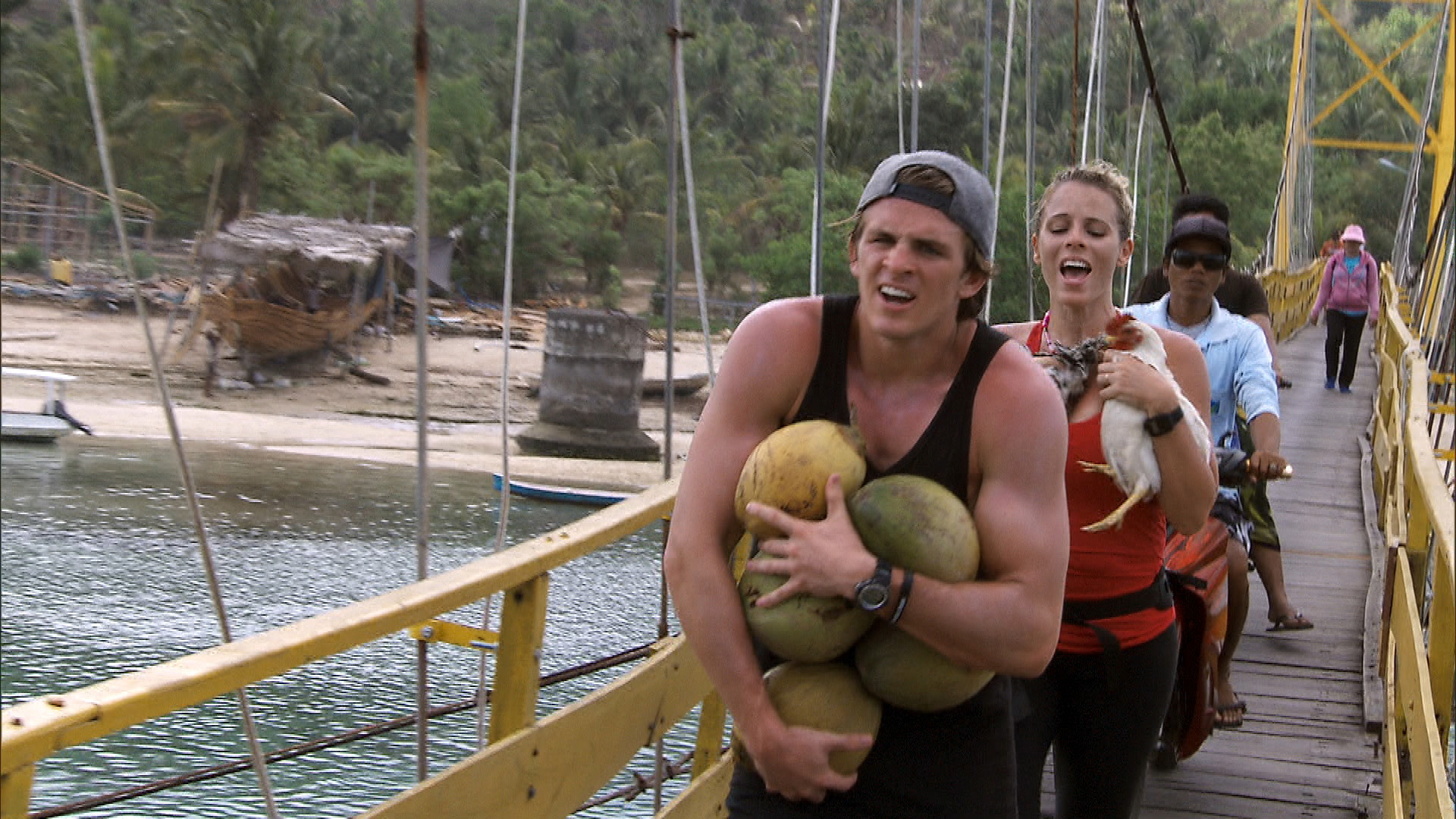 Cole and Sheri run across the bridge, carrying chickens and coconuts, to the Cenigan side.